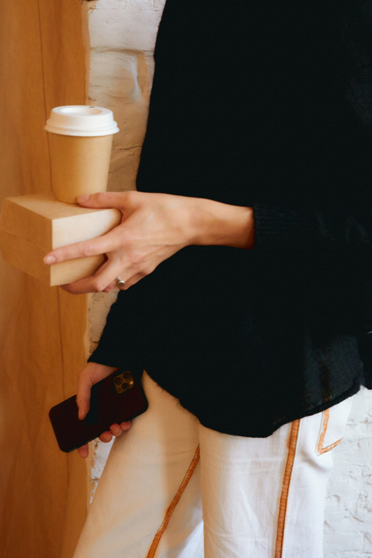 A hand holding a to-go coffee cup and a stack of kraft cup sleeves, phone in the other hand
