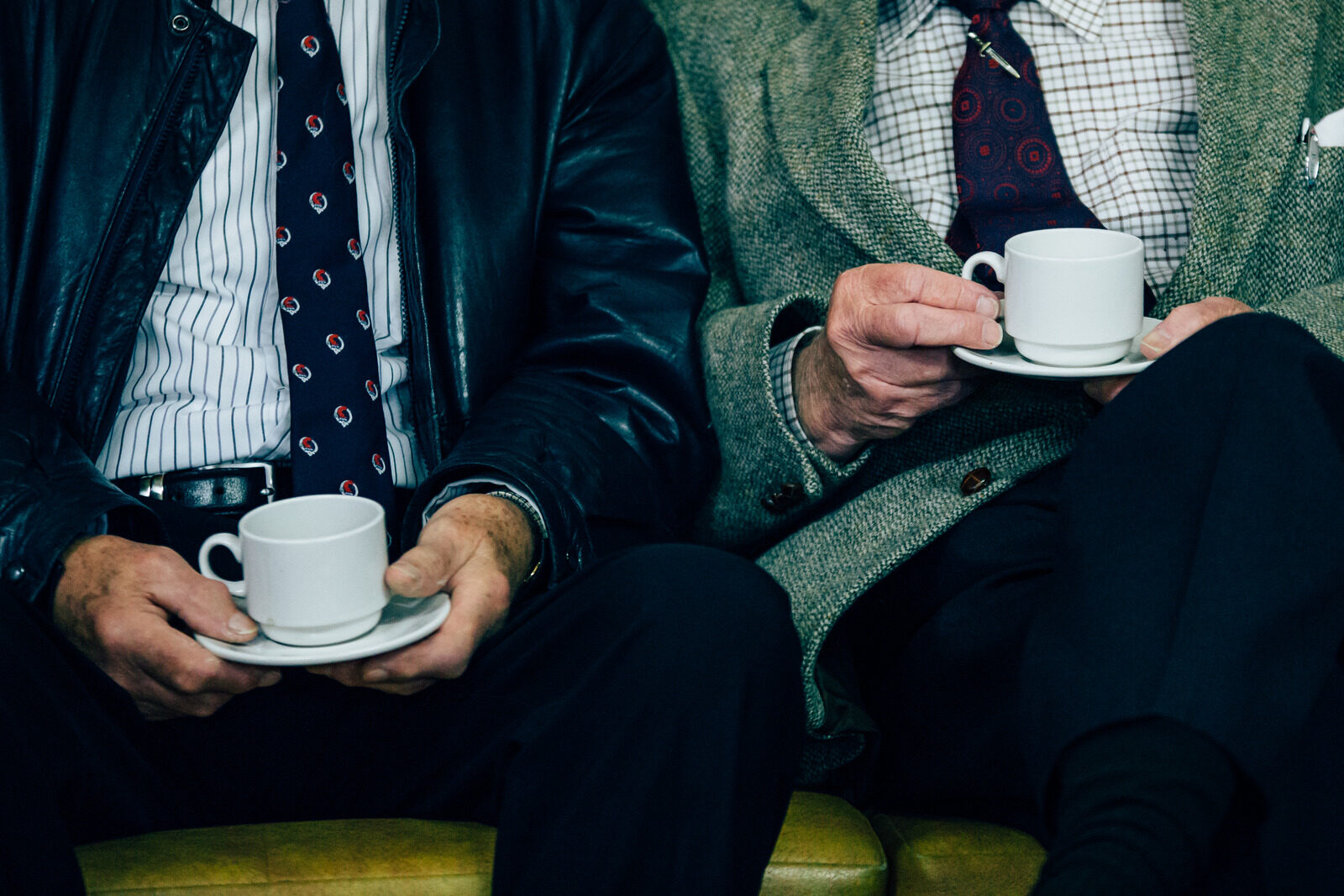 Two colleagues relaxed on a lounge couch, each holding a small espresso cup and saucer