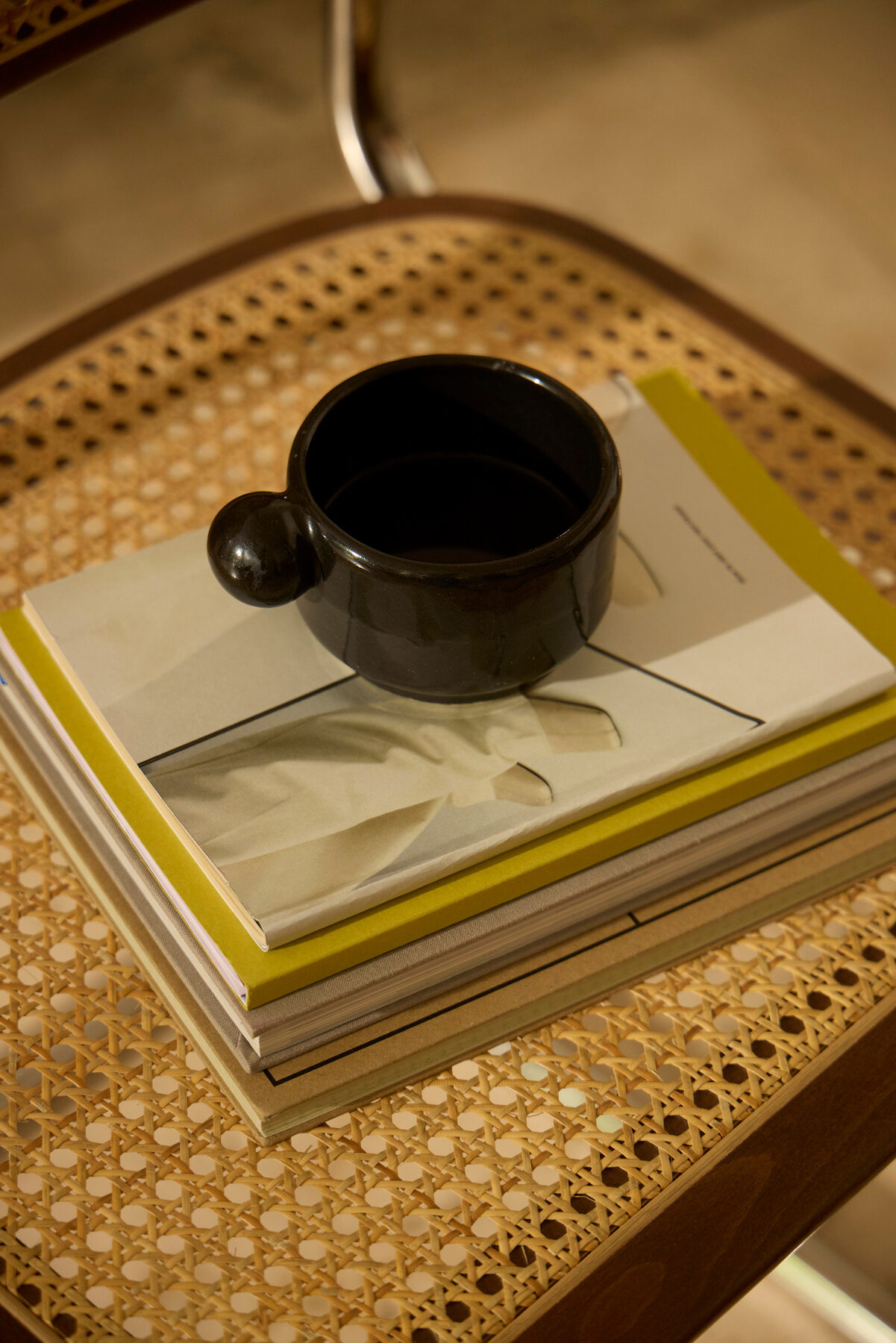 A dark ceramic cup resting on a stack of books on a cane chair