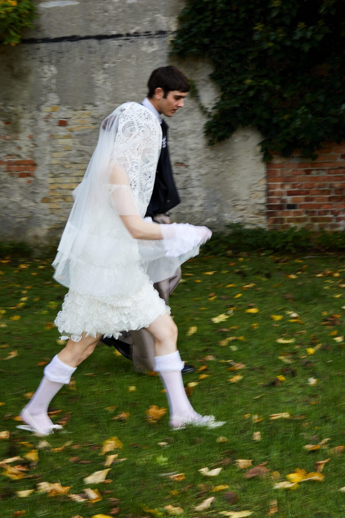 A guest in white crossing a leaf-strewn lawn at an autumn wedding