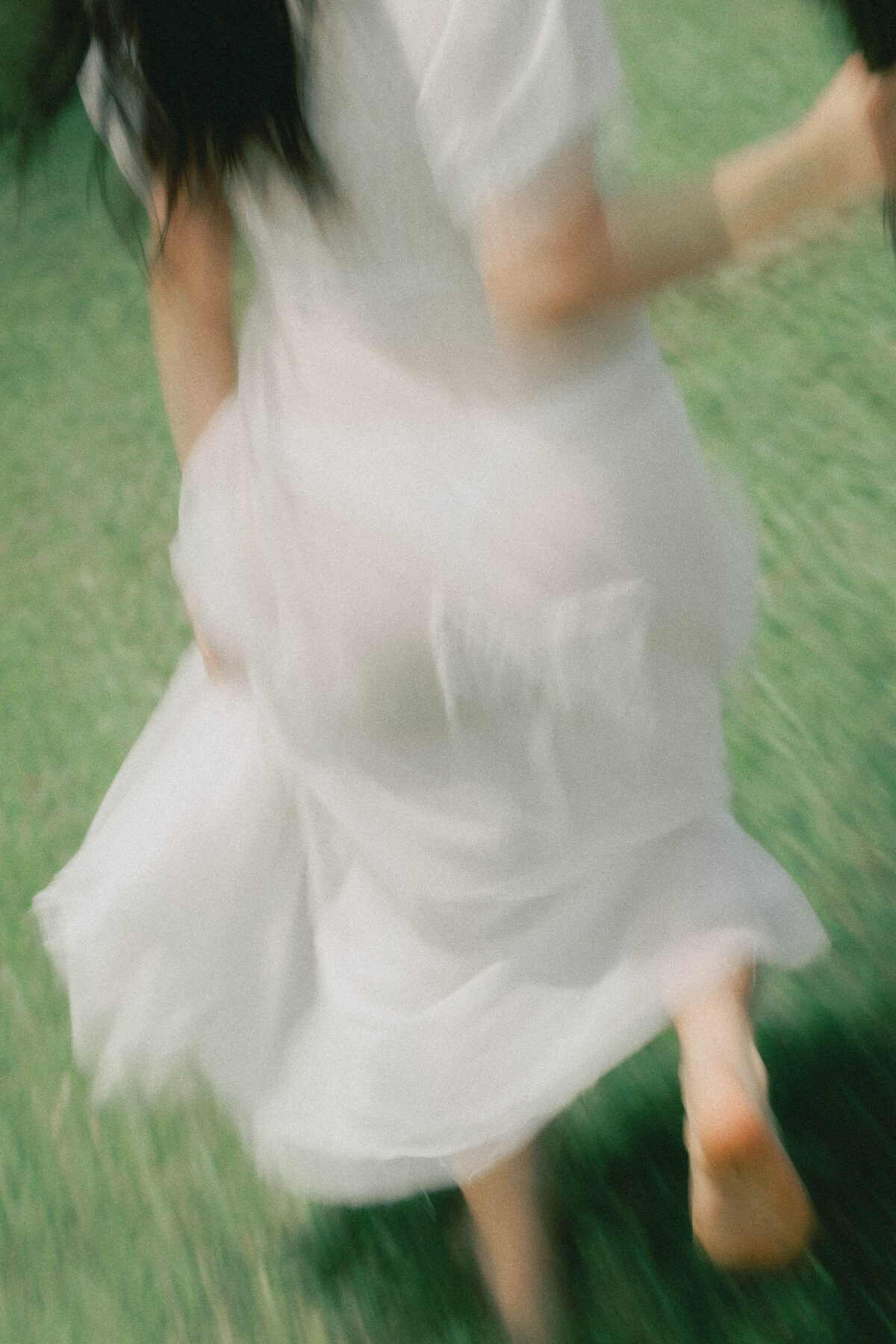 A guest in a white dress moving through sunlit grass at a wedding